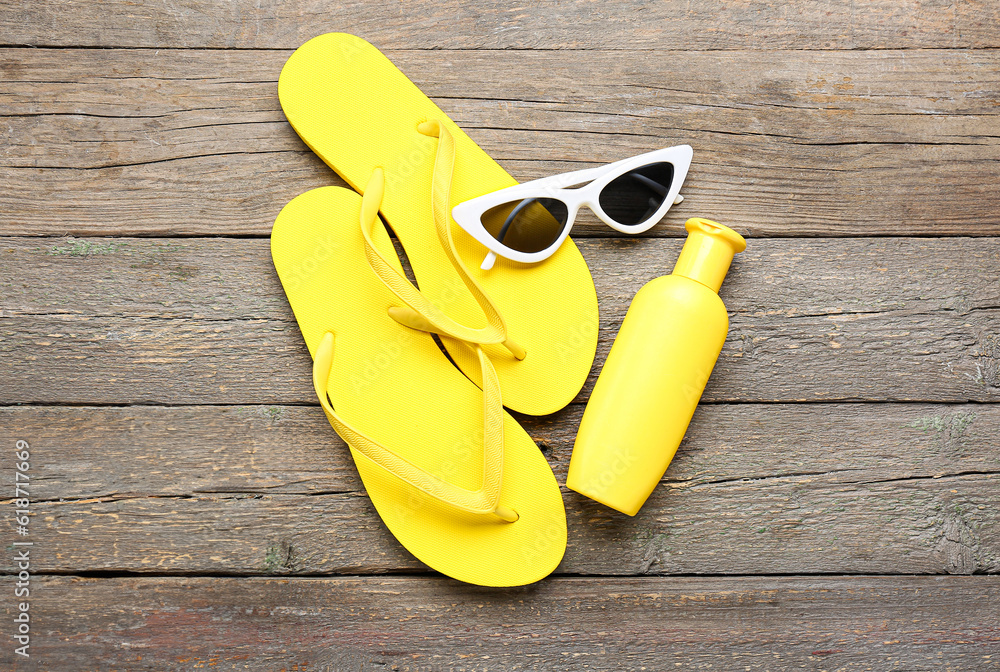 Sunglasses with flip flops and bottle of sunscreen cream on brown wooden background