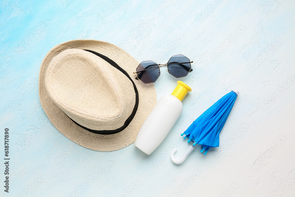 Wicker hat with sunglasses, mini umbrella and bottle of sunscreen cream on gradient background