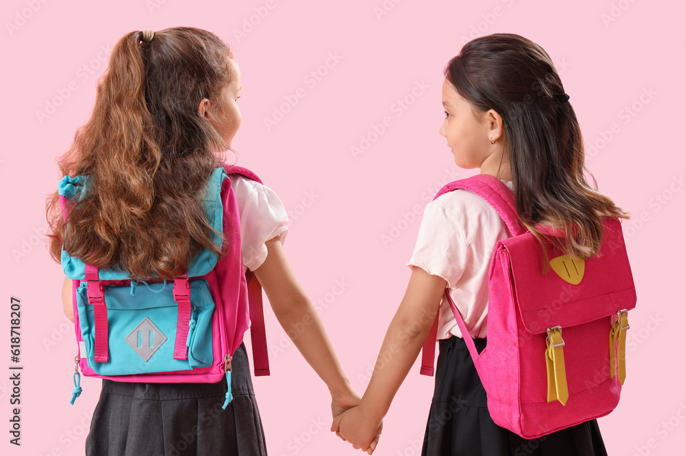 Little schoolgirls holding hands on pink background, back view