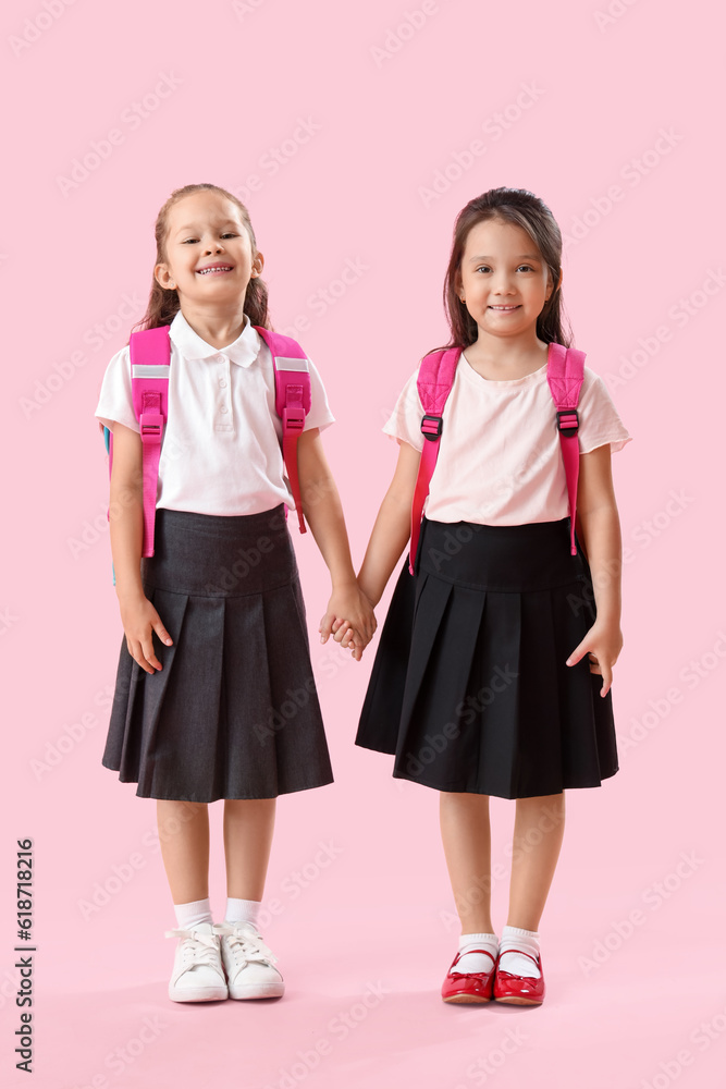 Little schoolgirls holding hands on pink background