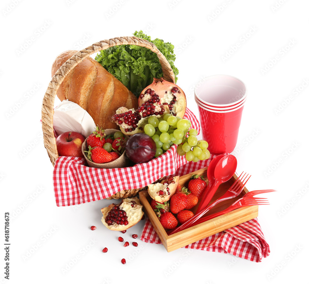 Wicker basket with tasty food for picnic and plastic tableware on white background