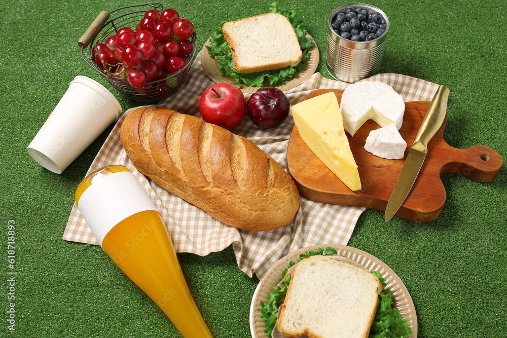 Tasty sandwiches, juice and food for picnic on green background