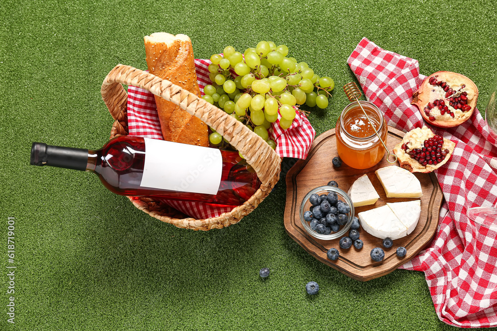 Composition with tasty food for picnic, honey and bottle of wine on green background