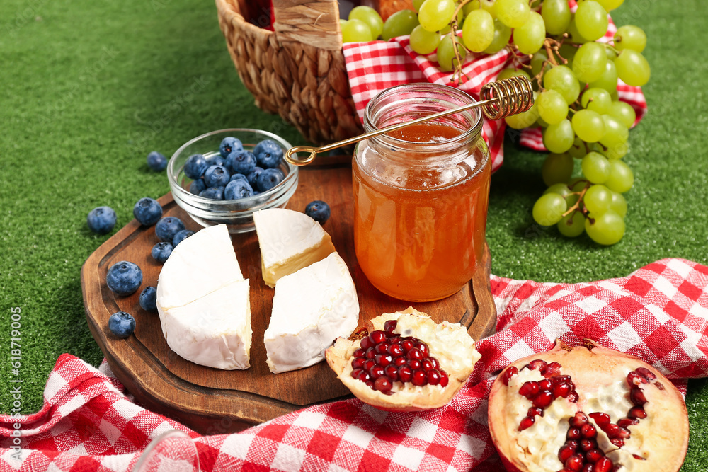 Board with tasty honey, cheese, blueberry and pomegranate on green background, closeup