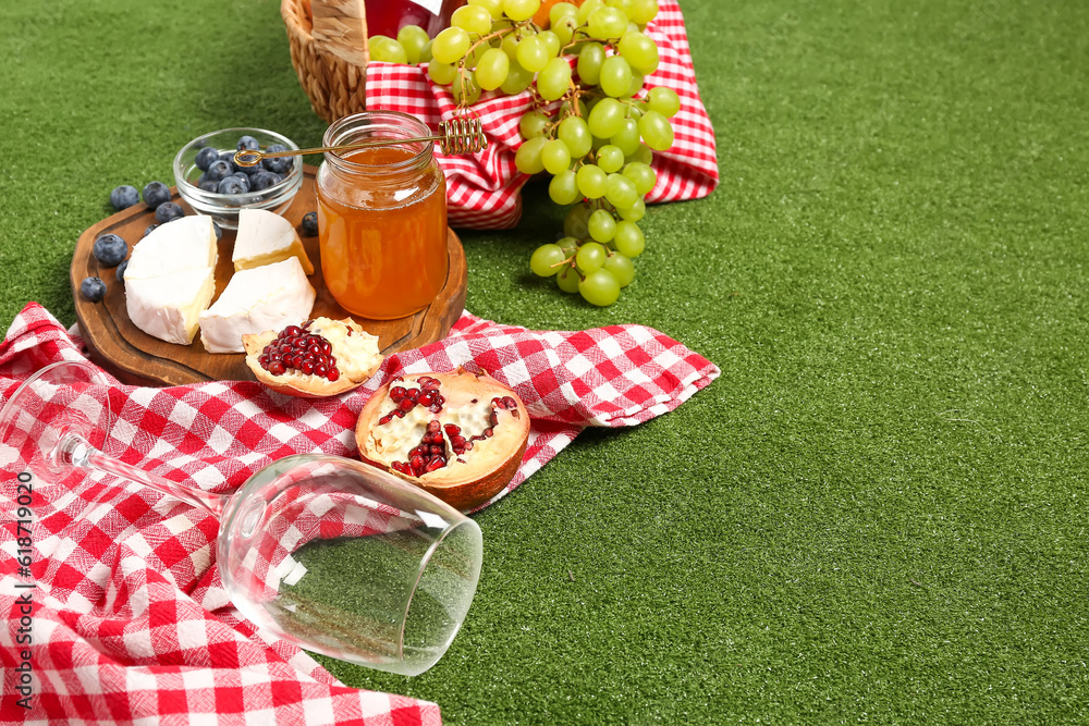 Board with tasty food for picnic and glass on green background, closeup