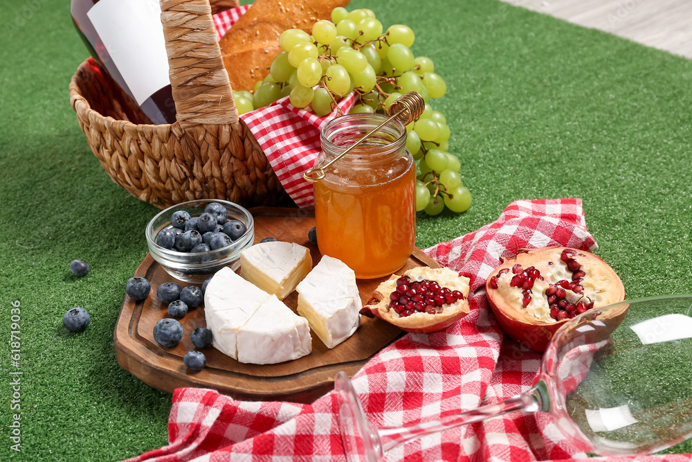 Board with tasty food for picnic and glass on green background, closeup