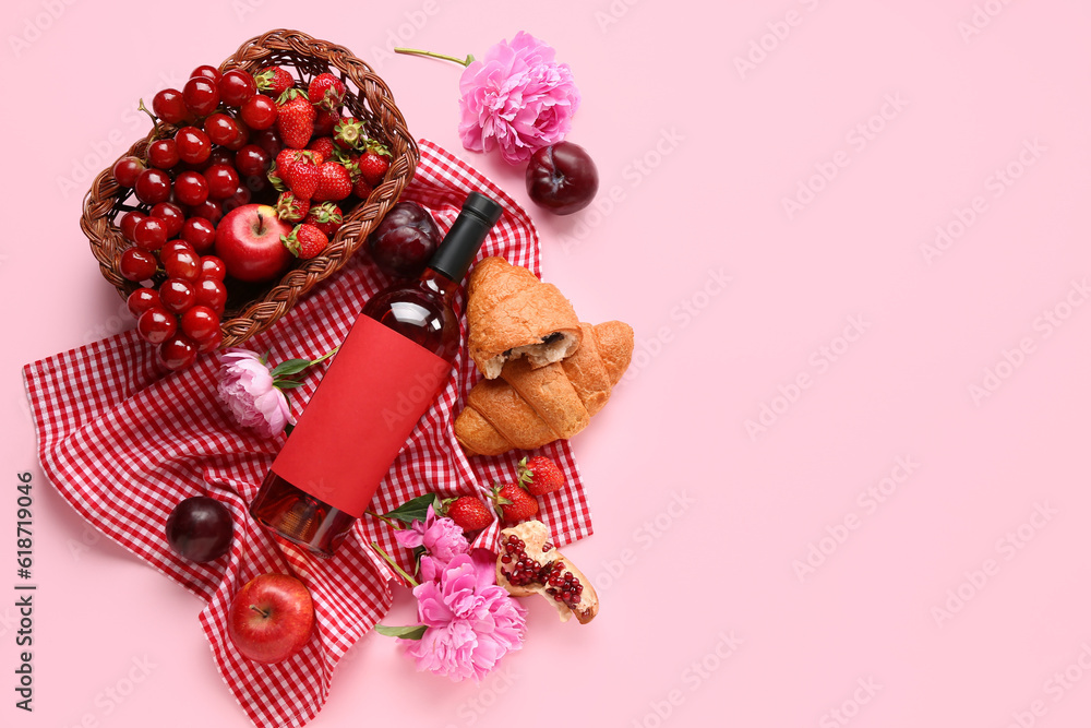 Composition with tasty food for picnic, bottle of wine and peony flowers on pink background