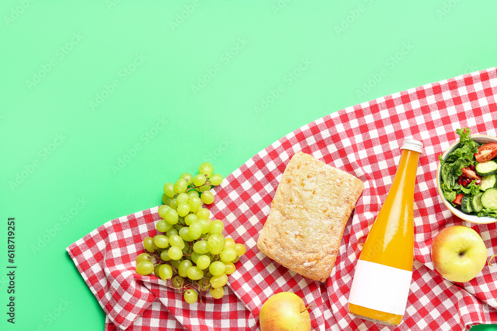 Bowl with salad, bottle of juice, bread and fruits for picnic on green background