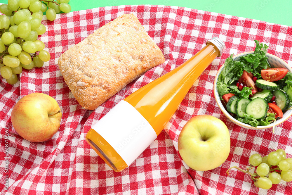 Bowl with salad, bottle of juice, bread and fruits for picnic on green background, closeup