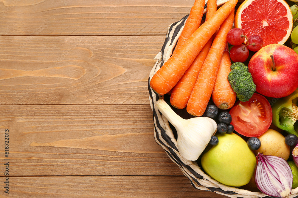 Wicker bowl with different fresh fruits and vegetables on wooden background, closeup