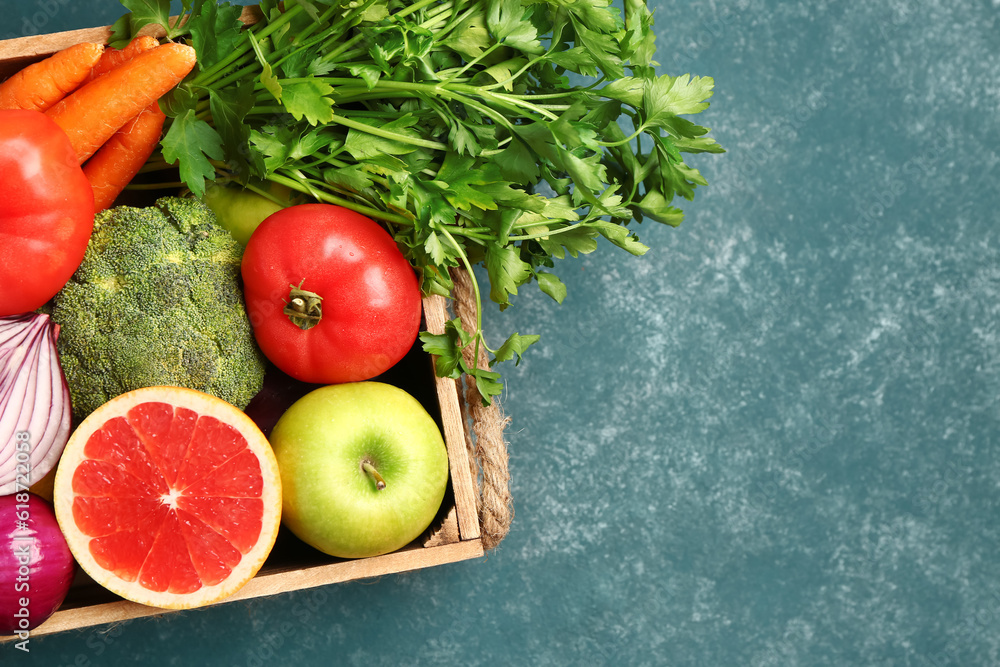 Wooden box with different fresh fruits and vegetables on green background, closeup