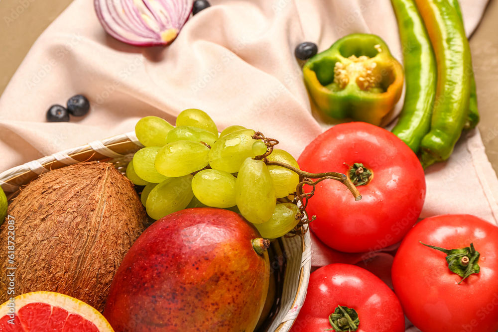 Wicker bowl with different fresh fruits and vegetables on brown background, closeup