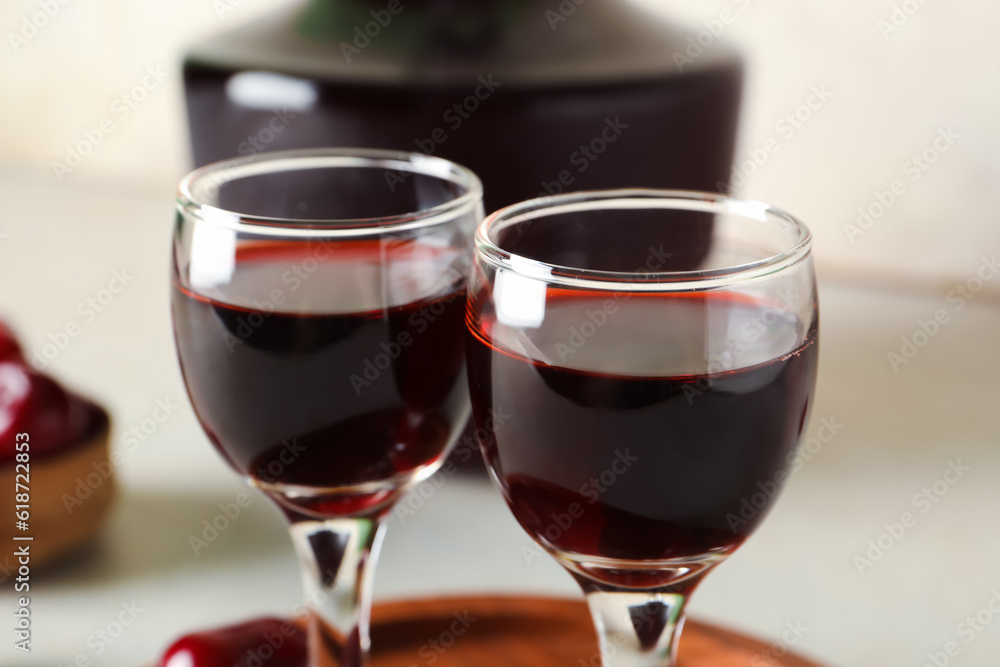 Glasses and bottle with sweet cherry liqueur on white background, closeup