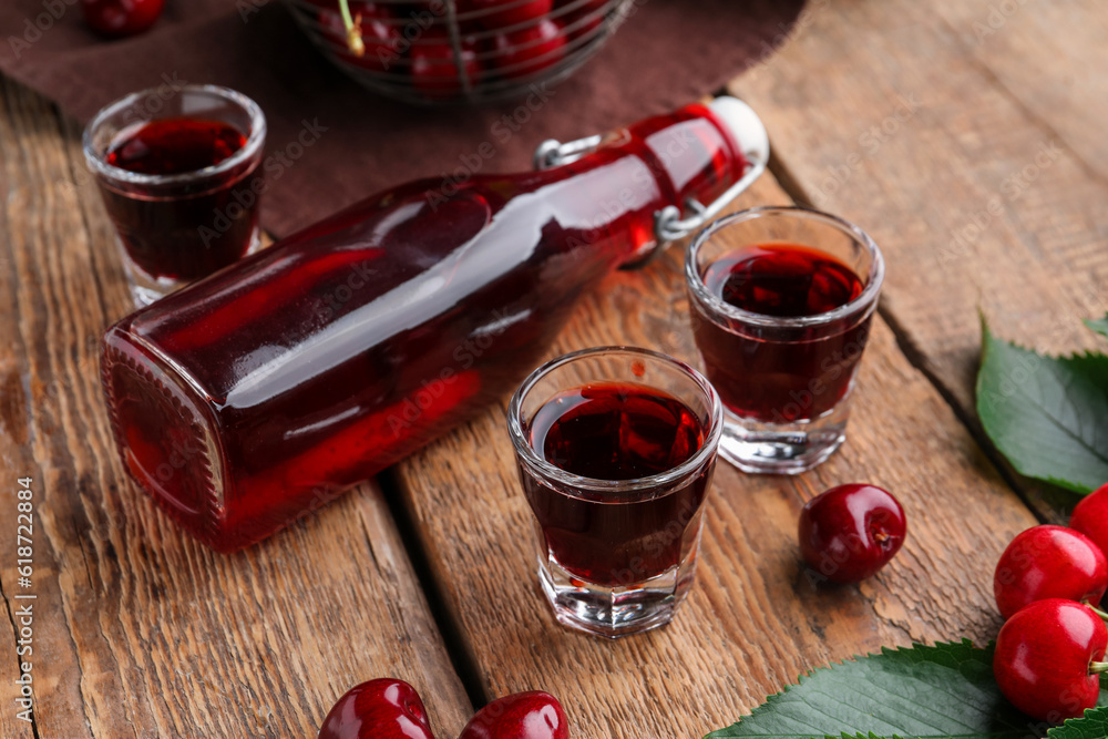 Shots and bottle with sweet cherry liqueur on wooden background