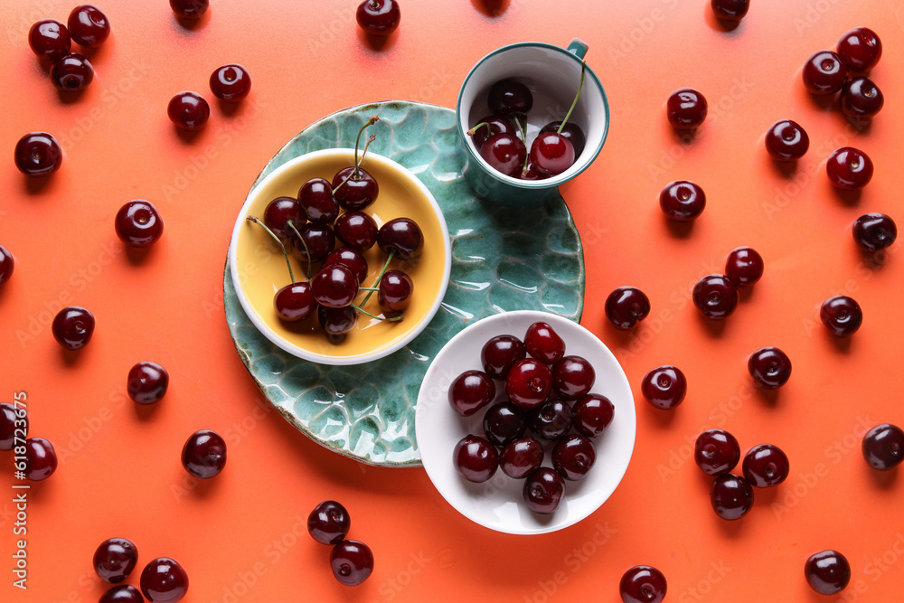 Plates and cup with sweet cherries on orange background