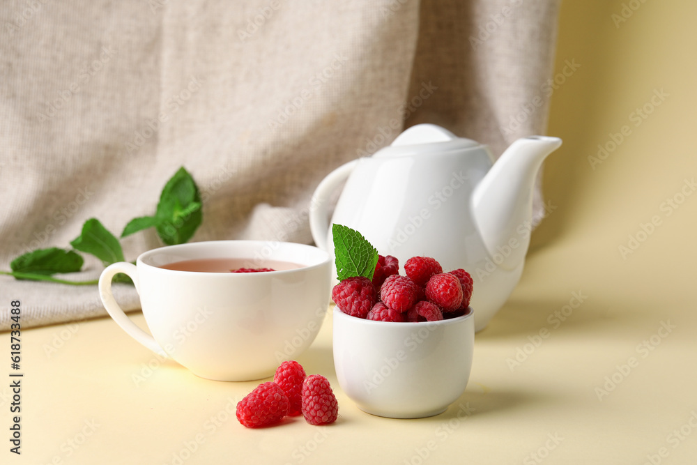 Bowl with fresh raspberries and cup of tea on yellow table