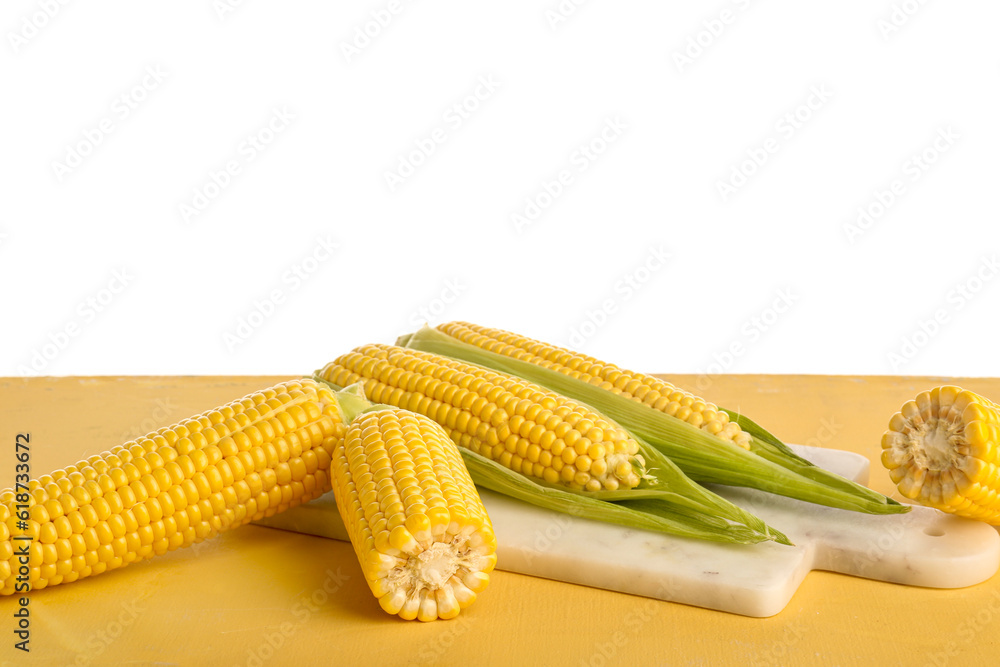 Board with fresh corn cobs on yellow table against white background