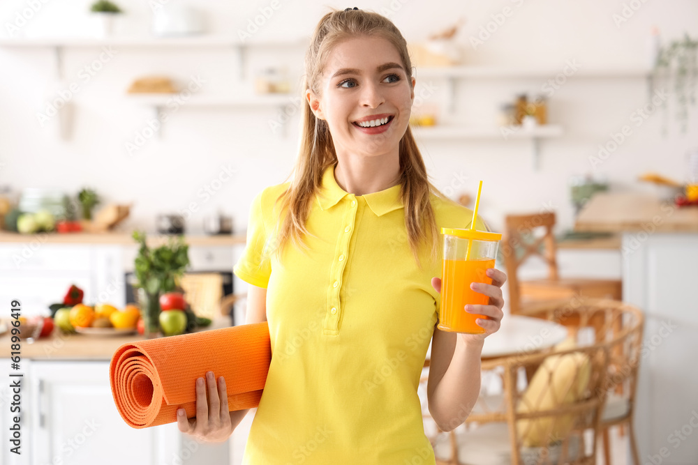 Sporty young woman with glass of vegetable juice and fitness mat in kitchen