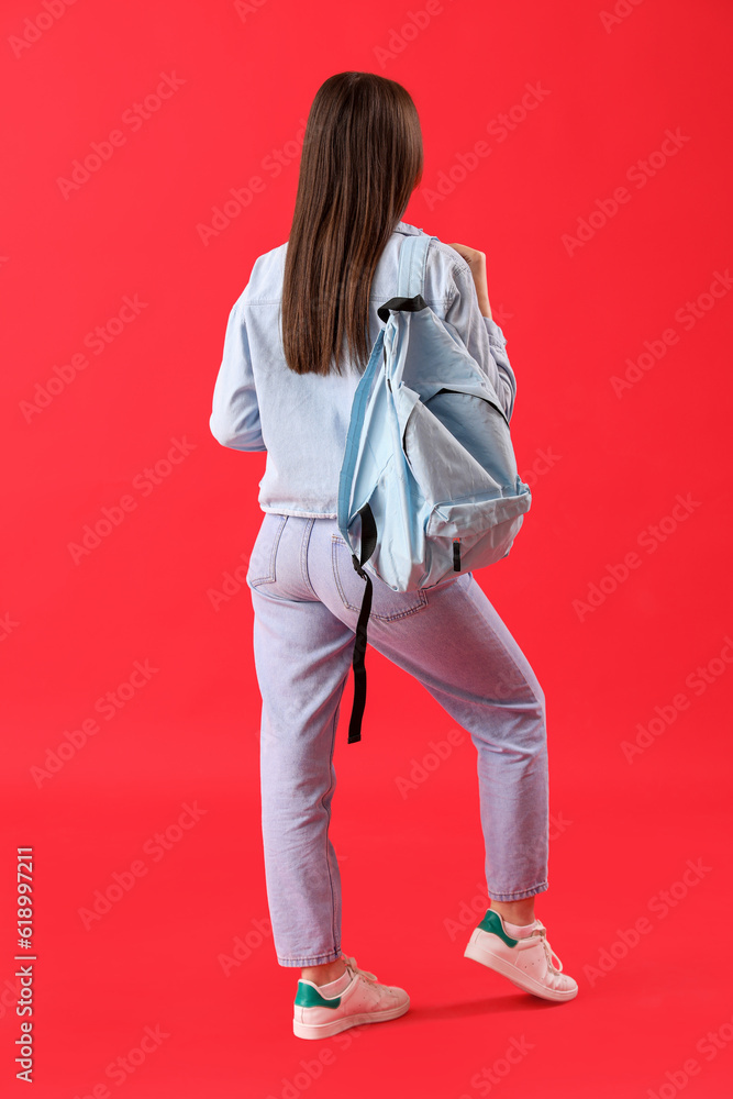 Female student with backpack on red background, back view