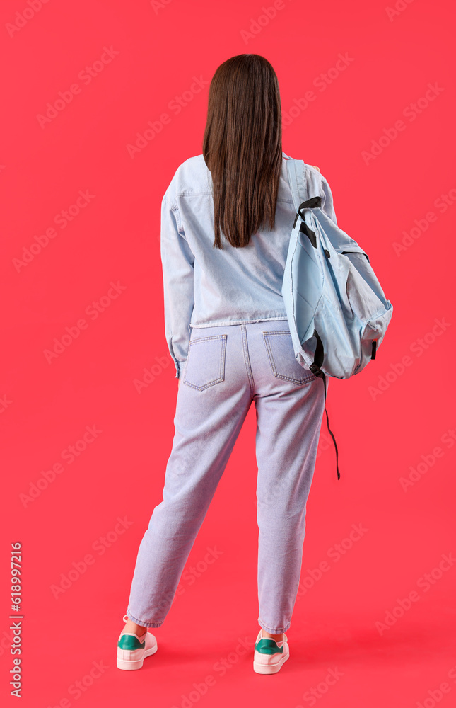 Female student with backpack on red background, back view