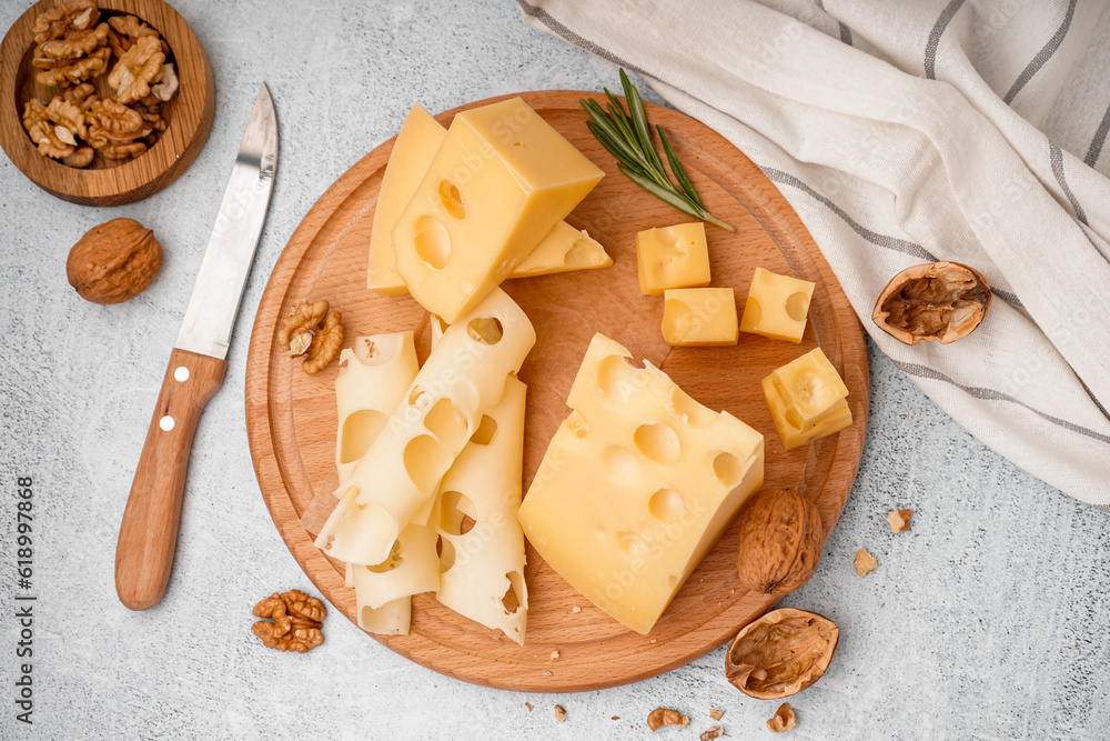 Board with pieces of Swiss cheese and walnut on white table