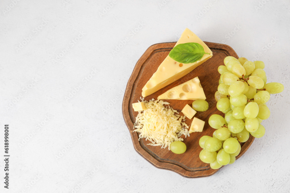 Wooden board with tasty Swiss cheese and grapes on light background