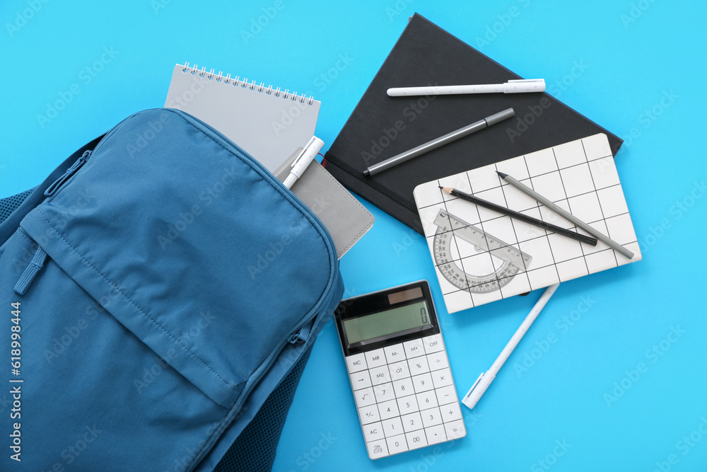 Color school backpack with notebooks, pencils and calculator on blue background