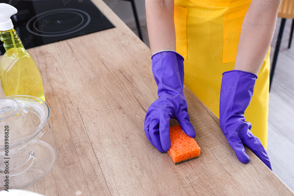 Woman in purple rubber gloves cleaning wooden countertop with sponge