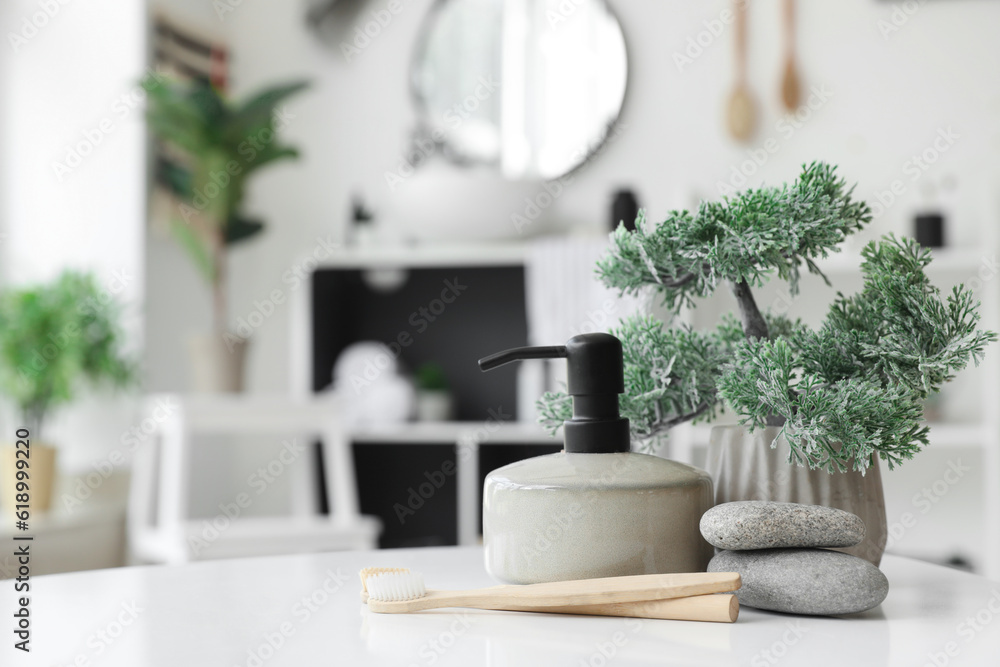 Toothbrushes, soap dispenser, houseplant and spa pebbles on white table in bathroom