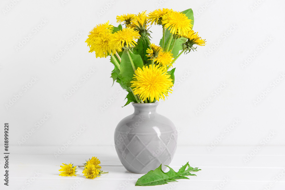 Vase with beautiful dandelion flowers on table near light wall