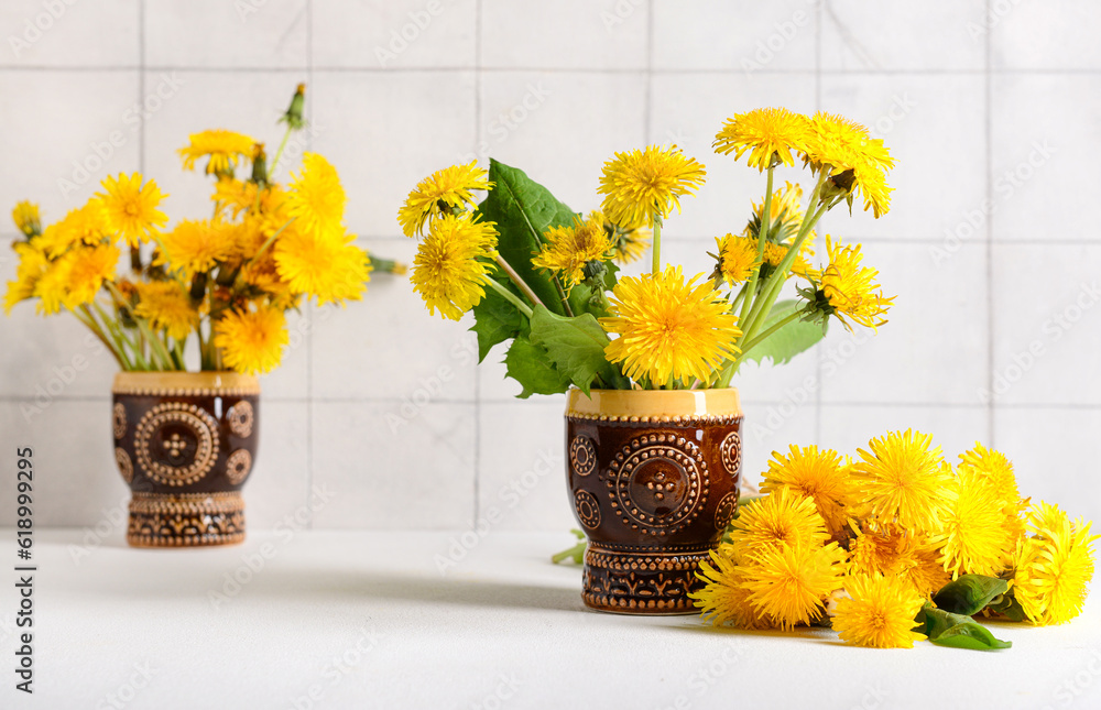 Vases with beautiful dandelion flowers on table near light tile wall