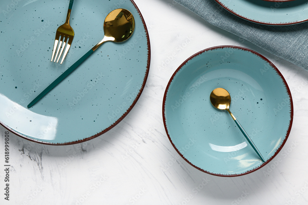 Table setting with clean plates, golden cutlery and napkin on white background