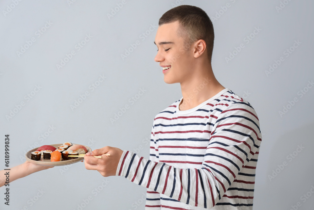 Young man and hand holding plate with tasty sushi on light background