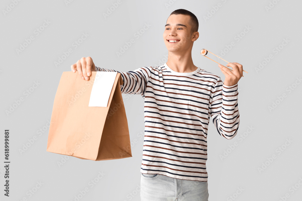 Young man with tasty sushi and paper bag on light background