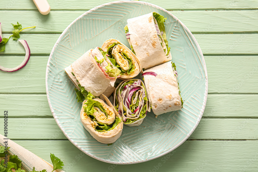 Plate of tasty lavash rolls with onion and egg on green wooden background