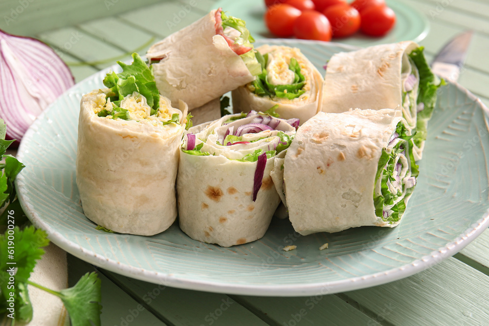 Plate of tasty lavash rolls with onion and egg on green wooden background