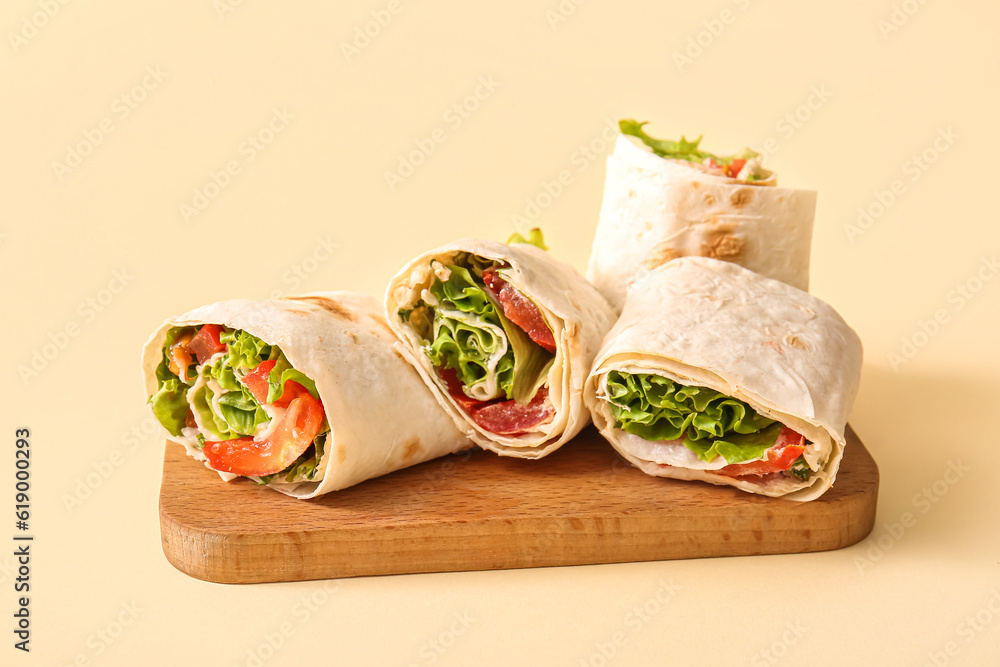 Wooden board of tasty lavash rolls with tomatoes and greens on beige background