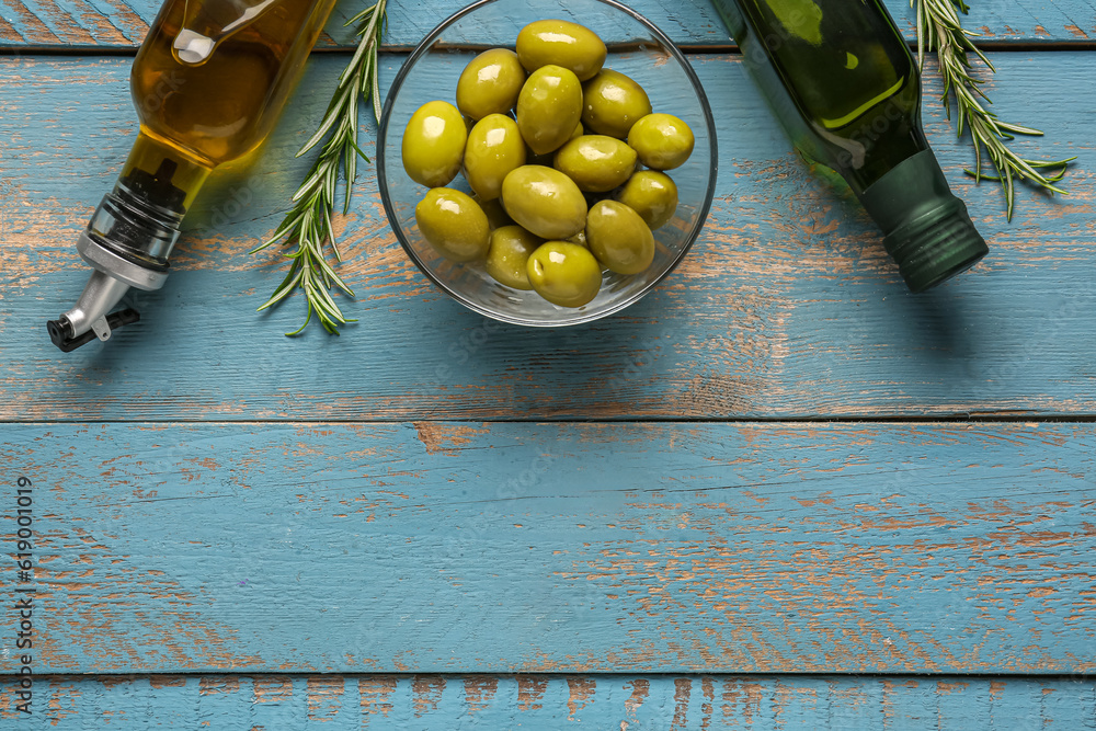 Bowl with ripe olives and bottles of oil on blue wooden background