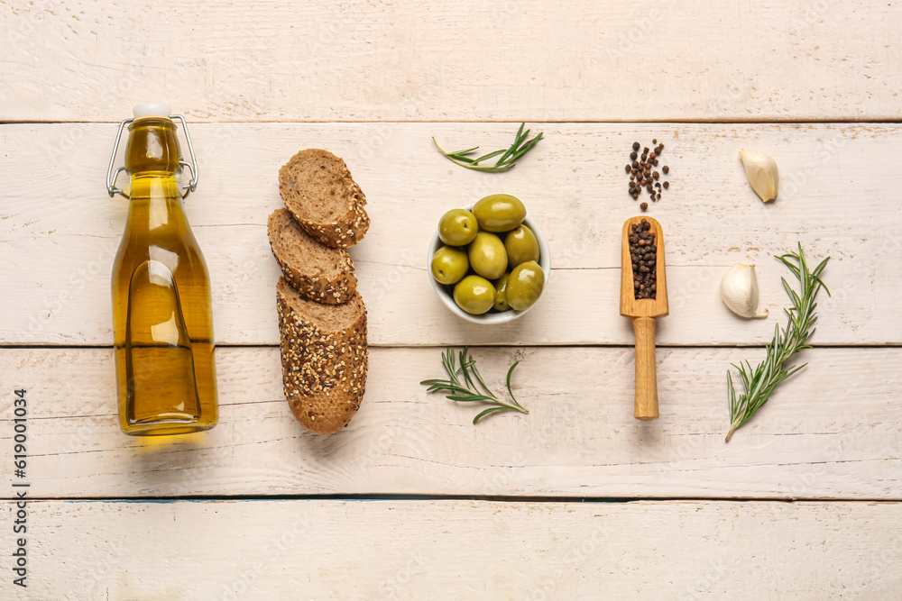 Bowl with ripe olives, spices, bread and bottle of oil on light wooden background