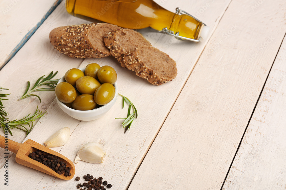 Bowl with ripe olives, spices, bread and bottle of oil on light wooden background