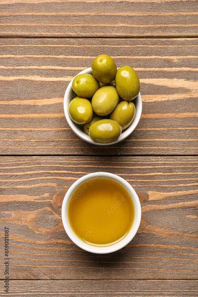 Bowls with ripe olives and oil on wooden background