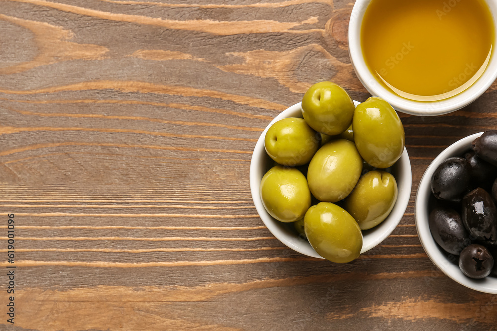 Bowls with ripe olives and oil on wooden background