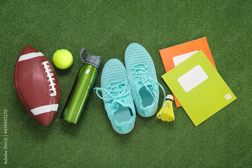 Sneakers with sport balls, bottle of water and notebooks on color background