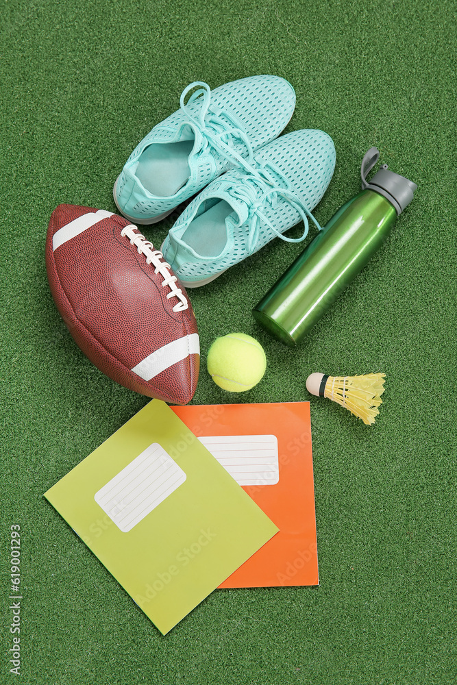 Sneakers with sport balls, bottle of water and notebooks on color background