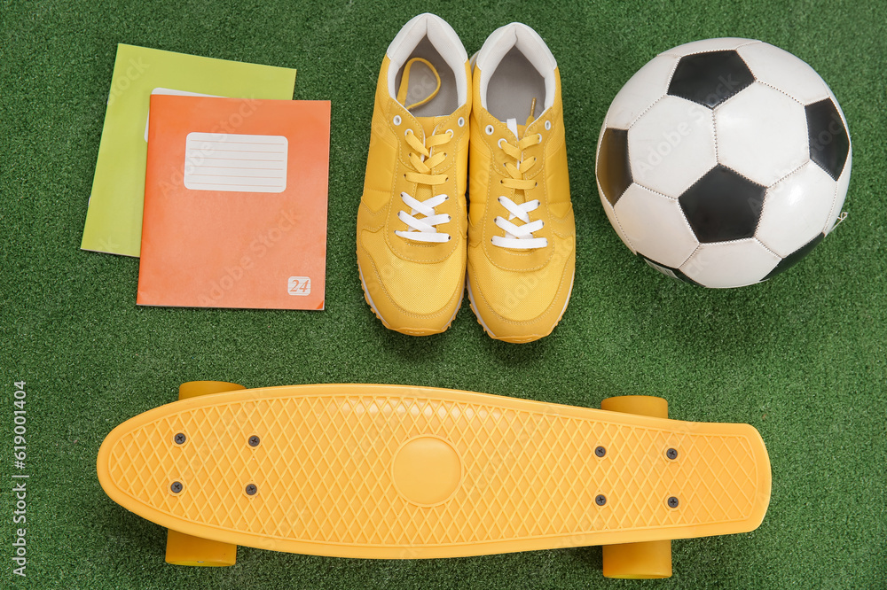 Sneakers with soccer ball, skateboard and notebooks on color background