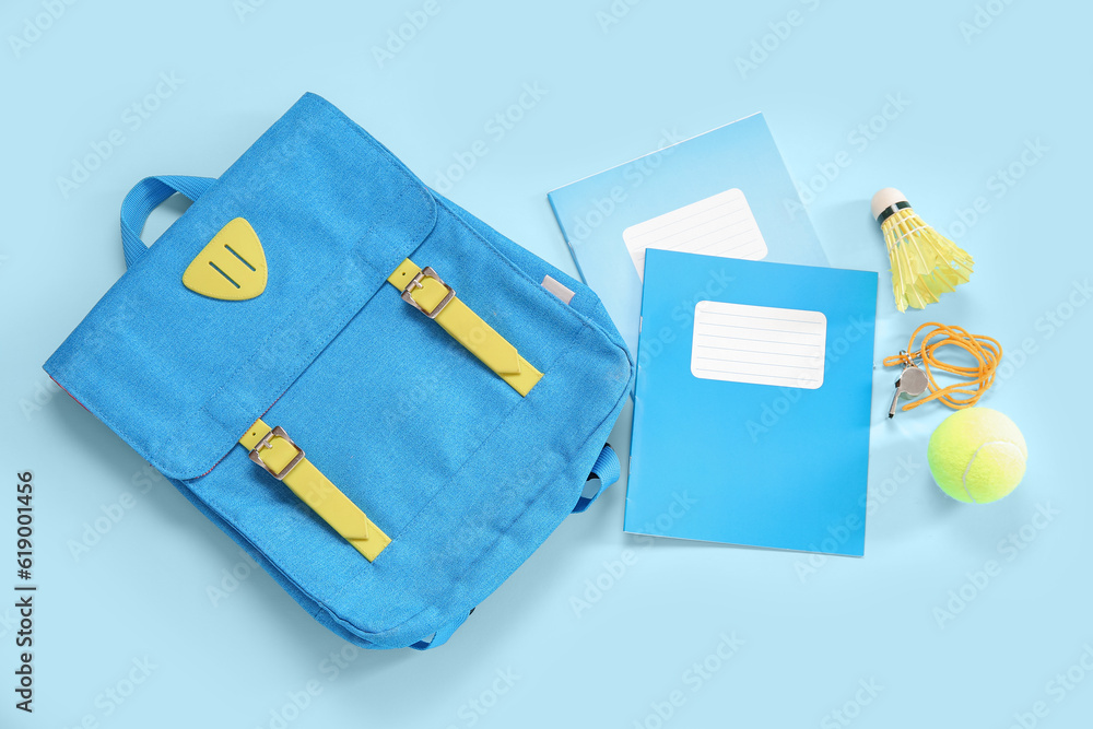 Backpack with tennis ball, whistle, badminton shuttlecock and notebooks on blue background