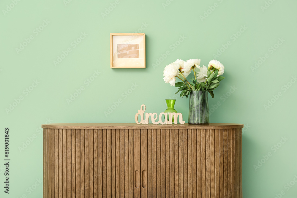 Vase of white peonies and decor in shape of word DREAM on dresser near green wall