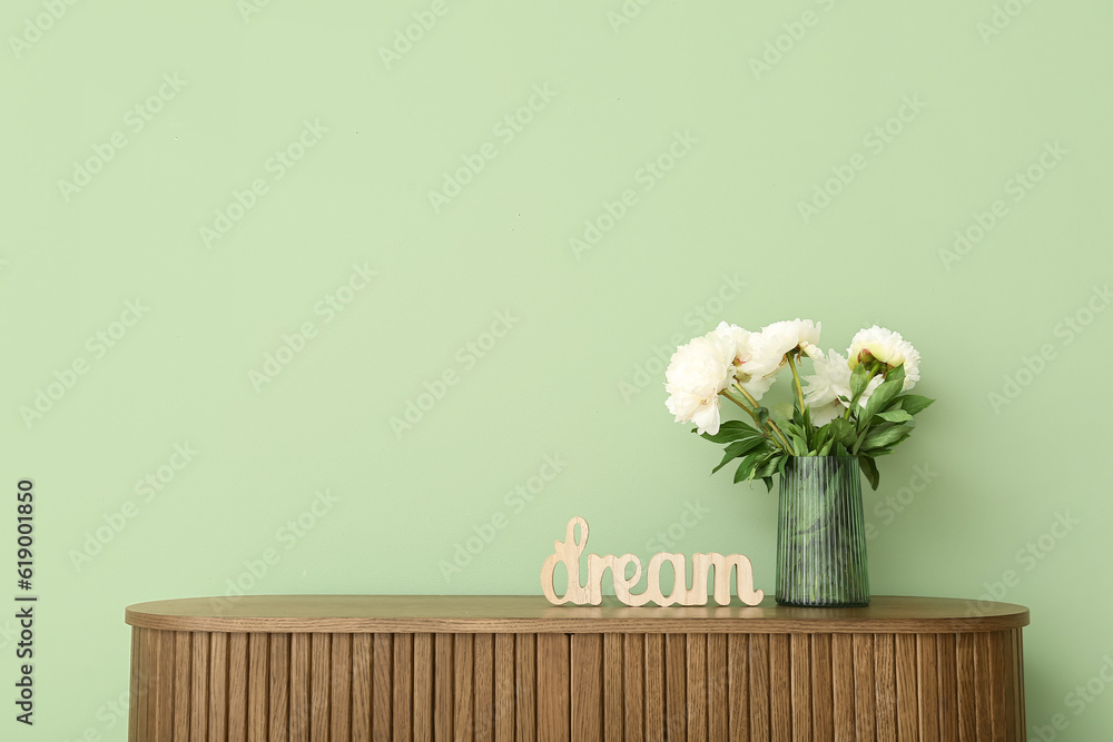 Vase of white peonies and decor in shape of word DREAM on dresser near green wall