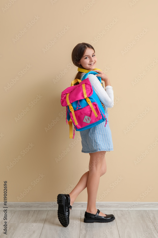 Little schoolgirl with backpack near beige wall