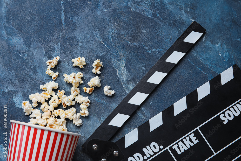 Bucket with tasty popcorn and clapperboard on blue background